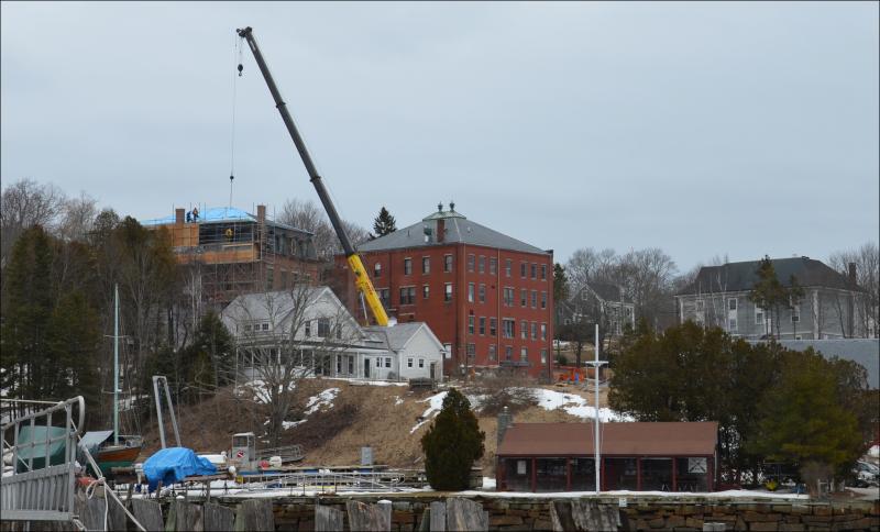 Looking north over Rockport Harbor in 2013 to the Shepherd Block, the large brick structure near Union Hall (which the crane operator is working on). The two buildings have undergone extensive renovations over the past decade by Leucadia Corp. and its subsidiary LLCs in the Midcoast since 2005. Now, a local family that invests in real estate plans to purchase it and keep it in commercial use. (Photo by Lynda Clancy)
